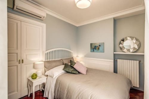 Camera da letto moderna in appartamento romano con letto bianco, arredamento beige, pavimento in legno e arredi contemporanei
