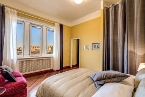 Camera da letto giallo brillante con vista panoramica su Roma, parquet e arredi moderni in appartamento nel centro storico