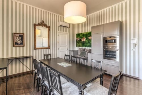 Elegante sala da pranzo in appartamento romano con tavolo nero, carta da parati a righe, cucina moderna e pavimenti in legno