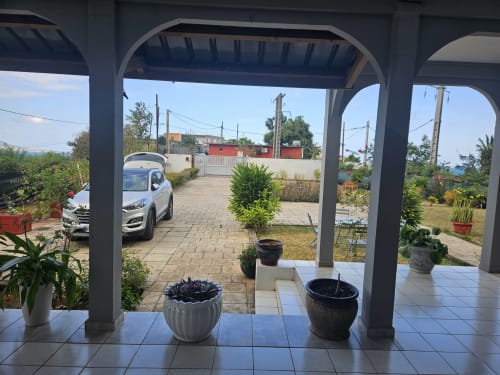 Patio du Kaz Kafe B&B à Mamoudzou avec véranda couverte, voiture garée, plantes en pots et vue sur la campagne