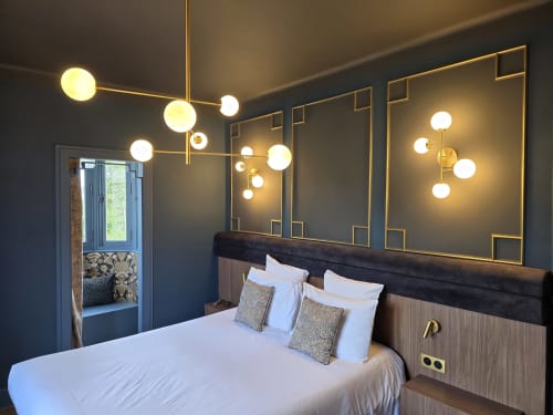 Chambre moderne au Castel Bayeux avec lit queen-size, suspensions globe en laiton et art mural miroir encadré or