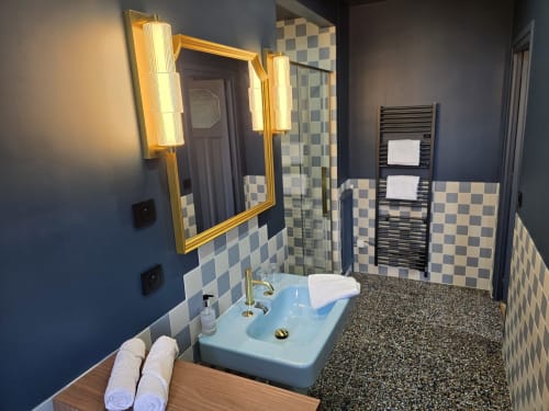 Salle de bain moderne au Castel Bayeux avec lavabo bleu clair, carreaux à damier, robinetterie dorée et sèche-serviettes chauffant