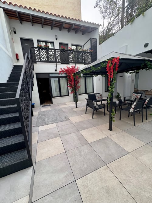 Patio interior de Be Gonfre Flats en el barrio de Ruzafa, Valencia, con zonas de descanso, plantas con flores rojas y escaleras a habitaciones