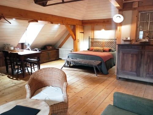 Chambre spacieuse à la Paulusmühle B&B à Soucht avec poutres apparentes, lit, bureau et fauteuil en rotin