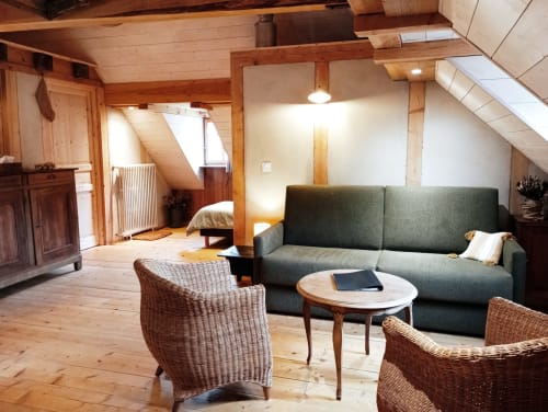 Spacieux séjour du gîte Paulusmühle avec canapé vert, fauteuils en osier et poutres apparentes à Soucht