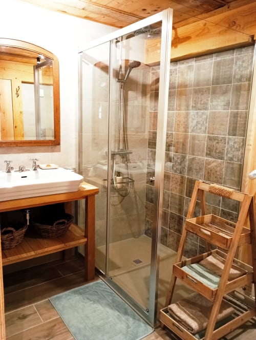 Salle de bains moderne du gîte Paulusmühle avec douche vitrée, meuble-lavabo en bois et plafond rustique