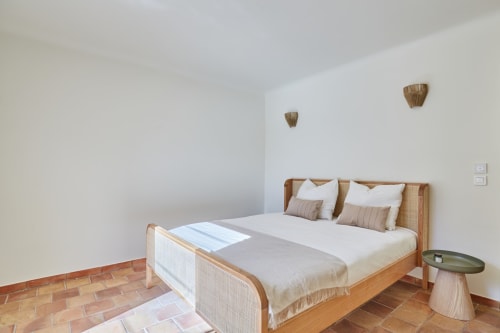 Chambre lumineuse avec lit en rotin, draps blancs, carrelage en terre cuite et décor mural tissé à CIRELINE-La Fontaine du Roy