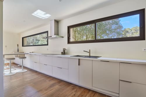 Cuisine moderne de villa avec meubles blancs, vue sur le jardin par grandes fenêtres, électroménagers en acier inoxydable à CIRELINE-La