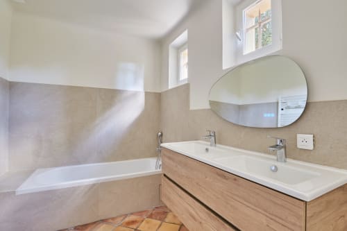 Salle de bains moderne de la villa Rognes avec double vasque, miroir ovale, baignoire et carrelage aux tons neutres