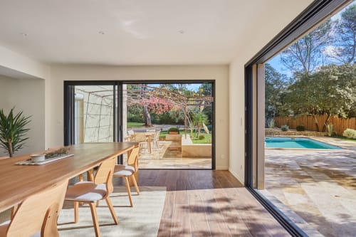 Salle à manger de villa moderne avec table en bois, vue sur le jardin par grandes portes vitrées et piscine visible à Rognes, France