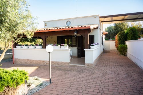 Modern terrace courtyard at L.H.A. property in Ferrara with white walls, potted flowers, and brick paving