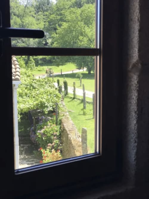Vista desde la ventana de los jardines del hotel O Lagar De Jesus en Padrón, con muros de piedra cubiertos de hiedra y frondosos terrenos verdes