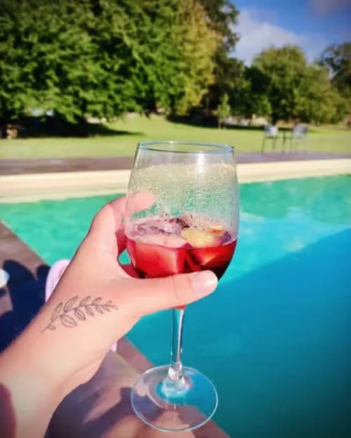 Mano sosteniendo sangría roja junto a la piscina reluciente del hotel O Lagar De Jesus en Padrón, España