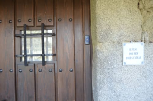 Puerta de madera con ventana de reja negra en la entrada del hotel O Lagar De Jesus en Padrón, España, con letrero visible