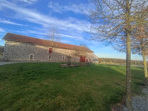 Stone farmhouse with red doors at Domaine de Beau Site in Peyrat-de-Bellac, surrounded by green lawn and bare trees under