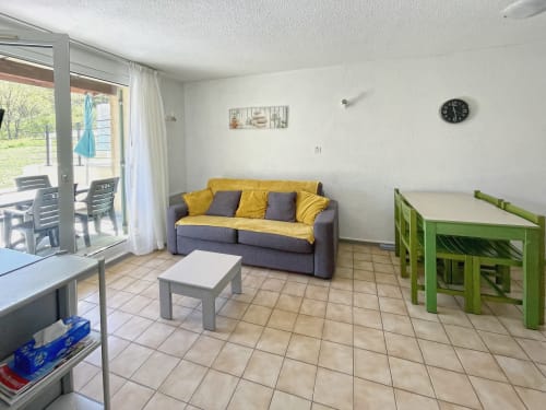 Salon lumineux de l'Appartement 124, Le Vallon des Sources, avec canapé gris, coussins jaunes, table verte et terrasse