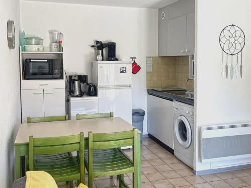 Cuisine de l'appartement Le Vallon des Sources avec chaises de salle à manger vertes, électroménagers blancs et équipements modernes à Digne-les-Bains
