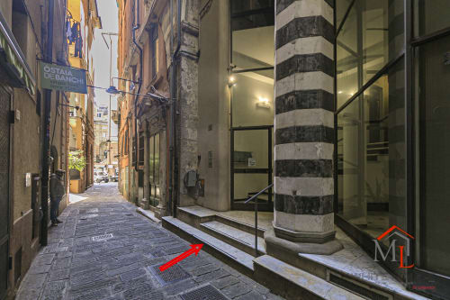 Stretto vicolo genovese con colonna in pietra rigata, edifici storici e ingresso dell'appartamento ML White House al tramonto