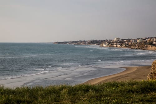 Spiaggia costiera suggestiva con sabbia dorata, onde gentili e edifici residenziali arroccati su scogliere che si affacciano sul Mediterraneo