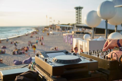 Attrezzatura DJ e mixer con vista sulla spiaggia, molo e folle al tramonto in location per evento