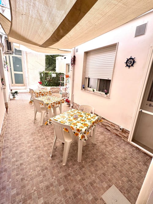 Area dining esterna presso Casa Vacanze La Coccinella a Trapani con sedie bianche, tovaglie girasoli, tenda ombreggiante e accenti rosa