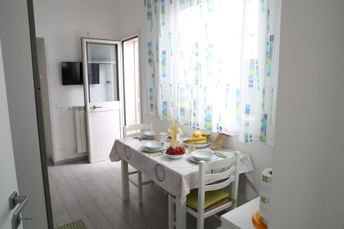 Bright dining area in Trapani apartment with white tablecloth, place settings, fresh fruit, and colorful patterned curtains