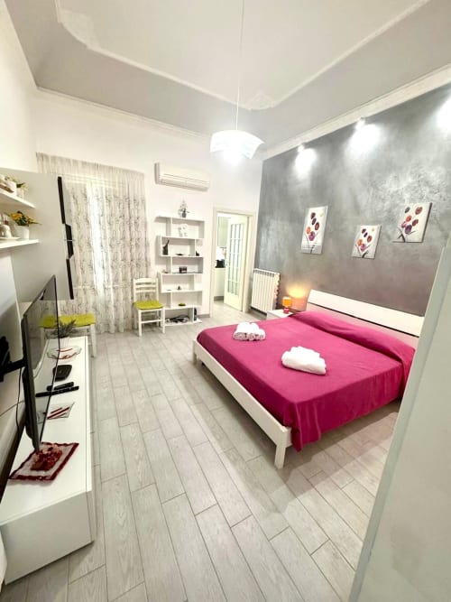 Modern bedroom with magenta bedding, gray accent wall, white furniture, and wood-look flooring in Casa Vacanze La Coccinella
