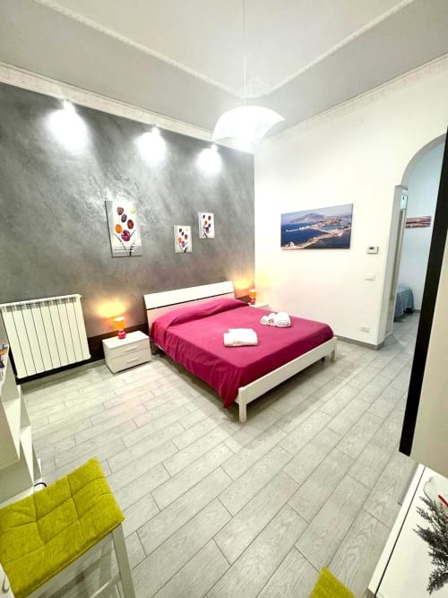 Modern bedroom with pink bedding, gray textured wall, white furniture, and bright pendant light at Casa Vacanze La