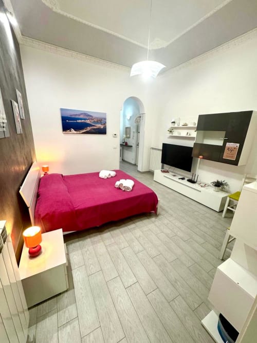 Bright modern bedroom with magenta bed, white furnishings, TV, and coastal artwork in Trapani apartment