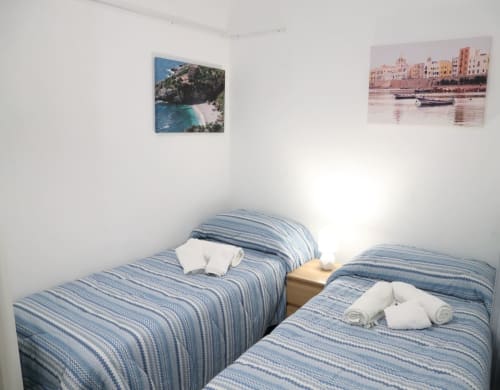 Two twin beds with blue striped bedding in bright Trapani apartment, decorated with coastal landscape photos
