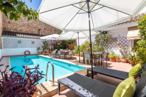 Casa Sibarita pool area with lounge chairs, white umbrellas, dining tables, and surrounding Mediterranean-style courtyard in