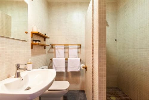Modern bathroom at Casa Sibarita with white sink, toilet, wooden shelves, towel rack, and walk-in shower with beige tile