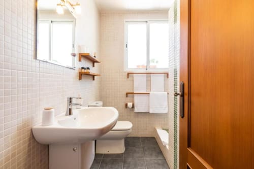 Modern bathroom in Casa Sibarita's Deluxe Double Room with white tile walls, sink, toilet, wooden shelving, and towel racks.
