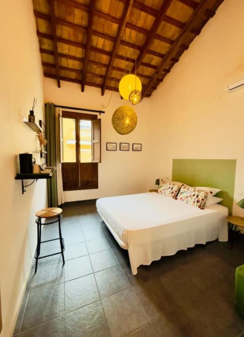 Premium Double Room at Casa Sibarita with green headboard bed, wooden beamed ceiling, yellow pendant lights, and city view in