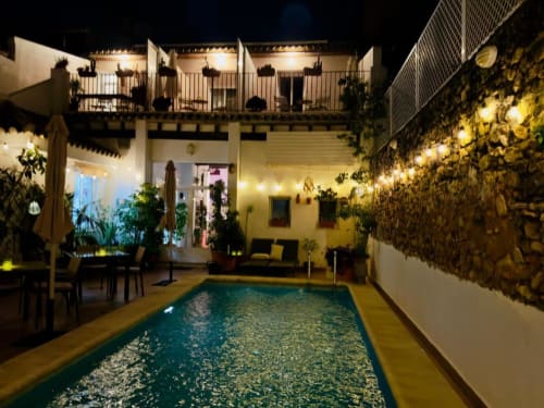Casa Sibarita courtyard at night with illuminated pool, potted plants, and multi-level white building with terraces in