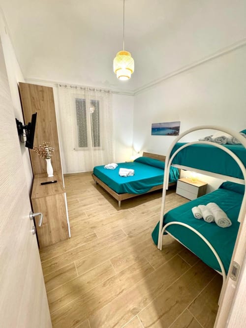 Bright bedroom at Casa Vacanze La Coccinella in Trapani with turquoise beds, wooden flooring, and modern amenities