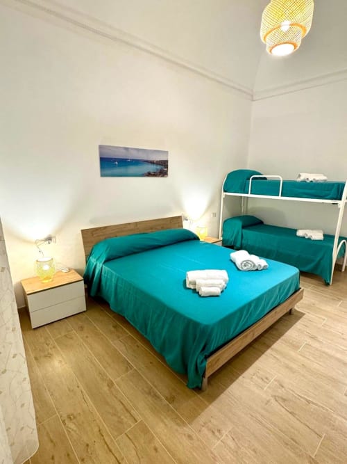 Bright bedroom with turquoise bedding, wooden floors, bunk bed, and white nightstand lamp at Casa Vacanze La Coccinella in