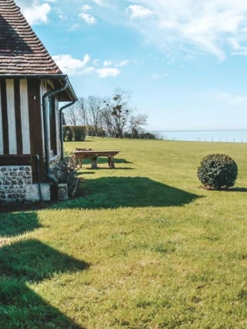Jardin du gîte La Girelle à Honfleur avec pelouse soignée, chaumière à colombages et vue sur l'eau au loin
