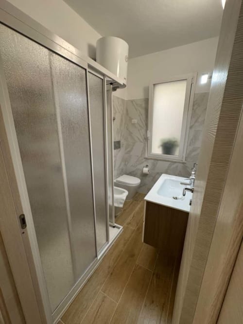 Modern bathroom at Casa Vacanze La Coccinella in Trapani with shower box, sink, toilet, and wood-look tiling