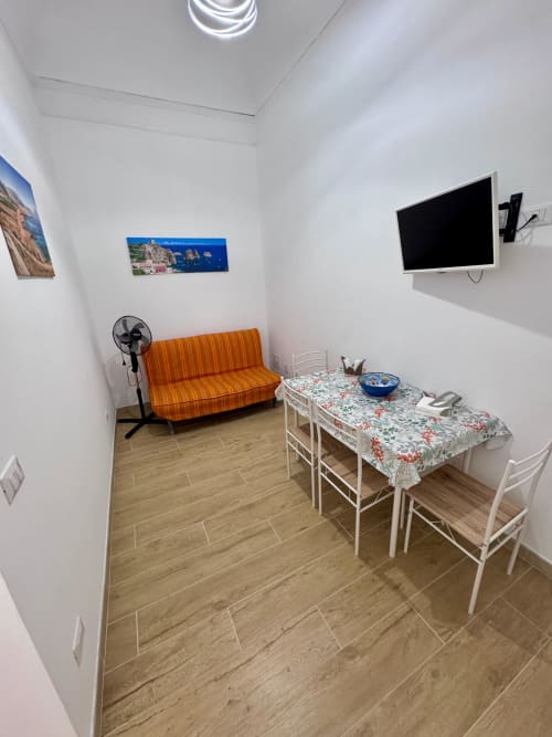 Bright apartment living space in Trapani with orange striped sofa, dining table, wall-mounted TV, and wooden flooring