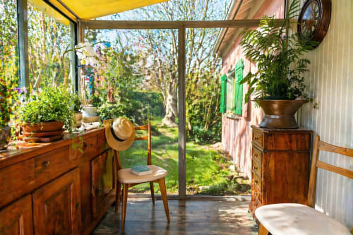 Sunny garden-view cottage conservatory at La Villa Malzy with wooden furniture, potted plants, and countryside views through