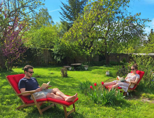 Couple relaxing in red chairs in La Villa Malzy's lush garden with blooming tulips and trees on a sunny day