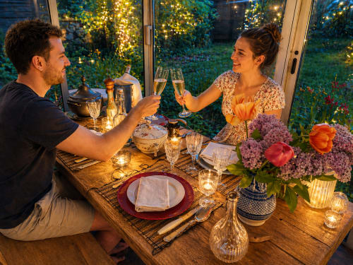 Couple toasting with champagne at elegant garden dining table at La Villa Malzy cottage, evening ambiance with flowers and