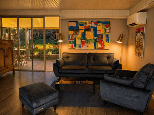 Modern living room at La Villa Malzy cottage with black furniture, colorful abstract art, garden views, and ambient lighting