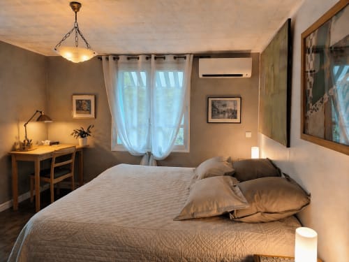 Cozy bedroom at La Villa Malzy cottage with queen bed, desk, AC unit, and garden view through curtained window