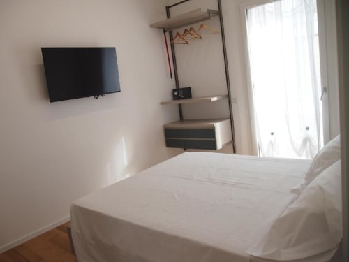 Camera Junior Suite moderna dell'Hotel Vienna Pesaro con letto bianco, TV a parete, scaffalature e balcone vista mare