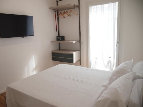 Camera Junior Suite moderna dell'Hotel Vienna di Pesaro con letto bianco, TV a schermo piatto, mensole a parete e vetrata