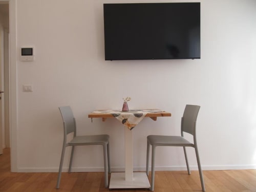 Moderna zona pranzo nella Suite Junior dell'Hotel Vienna con TV a parete, tavolo in legno, sedie grigie e pareti bianche
