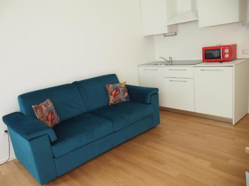 Divano letto blu con cuscini colorati nella suite junior dell'Hotel Vienna con angolo cottura e microonde rosso