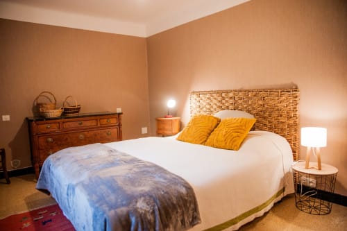 Chambre chaleureuse de la Maison de Marcelo à Carcassonne, avec tête de lit tissée, oreillers dorés et murs en terre cuite